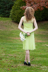 young woman with curly blond hair holding flowers with her back to the camera