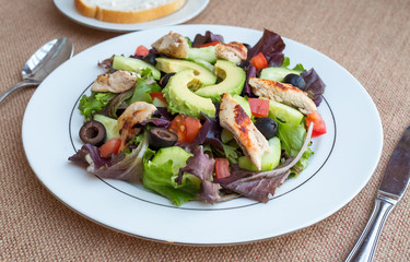 Chicken salad with avocado, mixed greens, cucumbers, tomatoes, and olives.