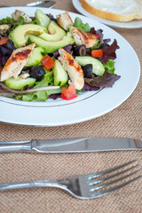 Chicken salad with avocado, mixed greens, cucumbers, tomatoes, and olives.