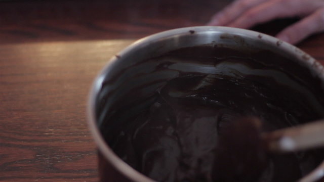 Closeup of a woman stirring melted chocolate in a pot with a wooden spoon