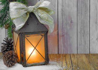 Rusty lantern with pretty bow on wooden table. Candle is glowing inside lantern.