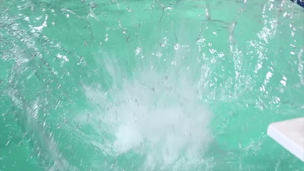 Slow motion HD footage of an Asian man with goggles jumping cannon-ball style into a pool, while facing forward