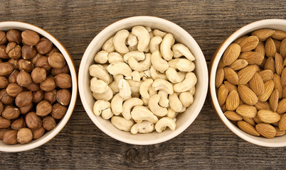 Almonds, cashew and hazelnuts in ceramic bowls on a rustic woode