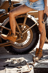 Naklejka na ściany i meble detail of a slim fit young woman with beautiful legs in yellow dusty working boots near motorbike fixing it with repair tools on a dusty roadside.