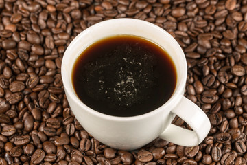Eine mit Kaffee gefüllte weiße Tasse steht inmitten von Kaffeebohnen