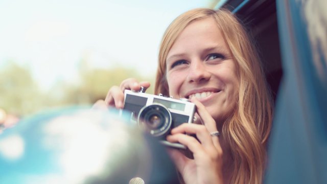 Handheld shot of blonde girl taking photo from car with a vintage film camera
