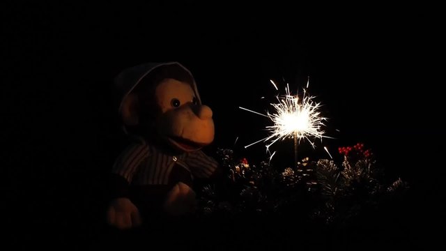 Новогодняя ночь. Бенгальский огонь горит, летят искры. Игрушка обезьяна, символ 2016 года по гороскопу. Новогодний, елочный венок. Темно. Рождество. Ожидание праздника