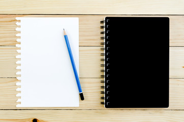 Black Notebook and blank paper with pencil on wooden table