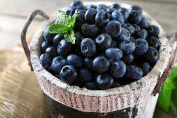 Tasty ripe blueberries with green leaves in bucket on table close up