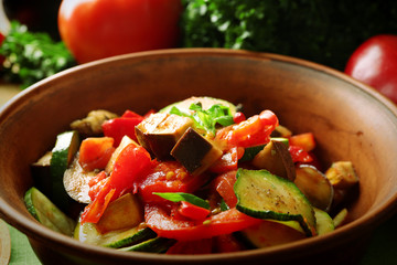 Tasty vegetarian ratatouille made of eggplants, squash, tomatoes in bowl on wooden table background