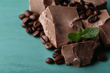 Milk chocolate pieces and coffee grains on color wooden background