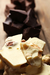 Black, milk and white chocolate pieces on color wooden background