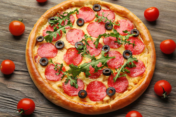 Tasty pizza with salami decorated with tomatoes on wooden background