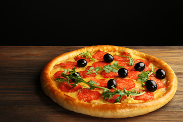 Tasty pizza with salami and olives on wooden table against black background