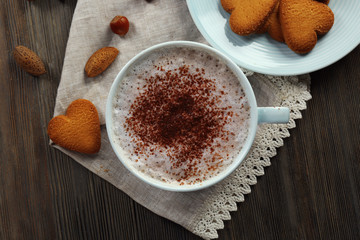 Cup of hot cacao on cotton serviette with cinnamon, almonds and heart shaped cookies, close up