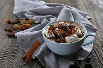 Cup of hot cacao with marshmallow, cinnamon and nuts on blue cotton serviette, close up