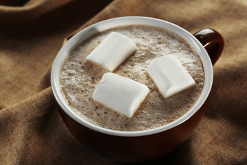 Cup of hot cacao with marshmallow on cotton serviette, close up