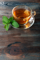 Glass cup of tea with mint leaves on wooden background