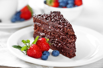 Chocolate cake with chocolate cream and fresh berries on plate, on light background