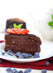 Chocolate cake with chocolate cream and fresh berries on plate, on wooden table, on light background