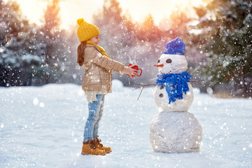 child girl plaing with a snowman - obrazy, fototapety, plakaty