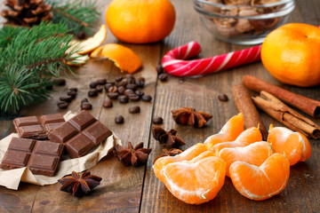 tangerines with chocolate and Christmas candy lying near a spruce branch with cone on wooden background