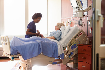 Hospital Nurse With Digital Tablet Talks To Senior Patient