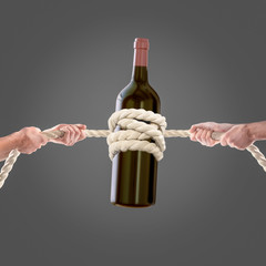 Hands of people pulling the rope bottle of wine on gray background. Competition concept