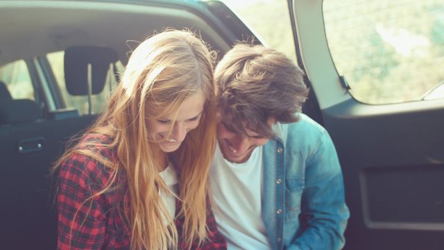 Handheld shot of couple sitting in car trunk checking map
