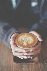Woman hand hold cup of coffee latte on the wood texture   in vintage color tone