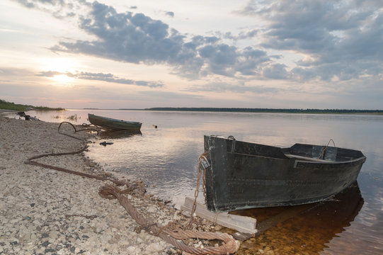 Two laid up wooden boats against panorama of Severnaya Dvina river in sunset background. 
