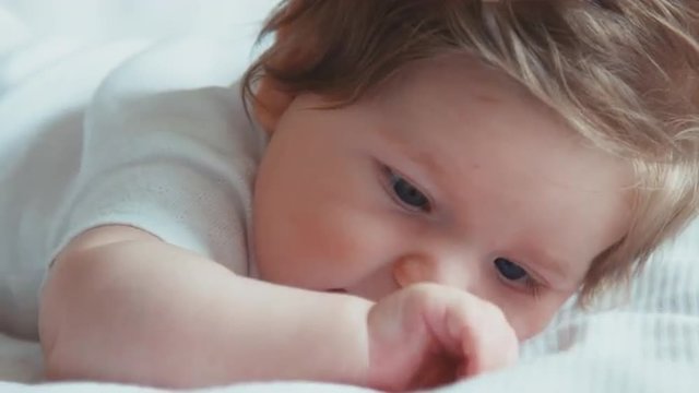 Closeup portrait of blue-eyed newborn baby girl boy lying on the bed. Child tries to raise his head