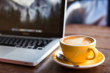 Hot art Latte Coffee in a cup and laptop on wooden table