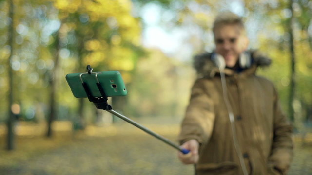 Boy holding selfie stick and doing photos in the park
