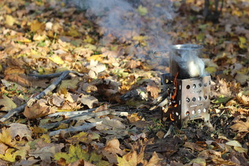 Tourist mini stove with a mug in the autumn forest