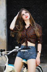 Fototapeta na wymiar Beautiful girl with long hair is posing on bicycle on the street