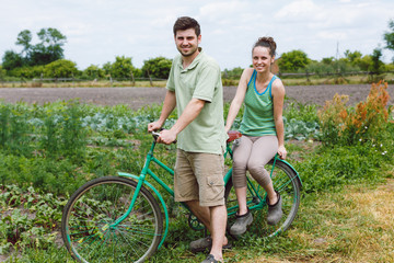 Obraz premium Young brunet woman is sitting on the green retro bicycle and handsome man is standing near her