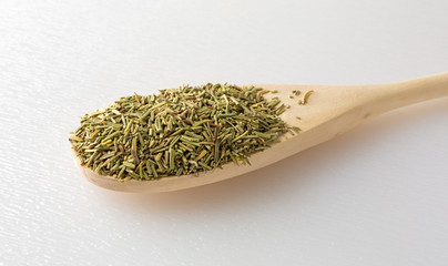 Dried rosemary leaves in spoon on a cutting board