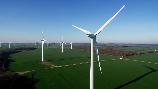 Reveal aerial clip of wind turbine farm in rural landscape shot in late evening with long shadows.