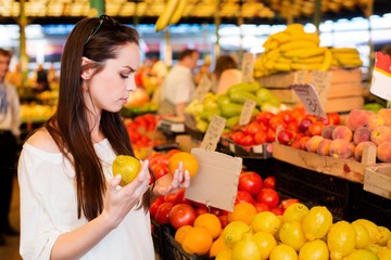 Young brunette woman is holding lemon and orange in her hands