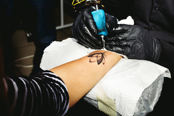 Man wearing on black gloves and jacket, making a tattoo of lotus flower on the girl's arm