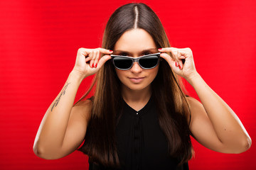 Naklejka premium Serious young woman, with long dark hair, in black blouse and sunglasses, looking at camera
