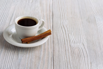 Cup of coffee with cinnamon stick on a white wooden background