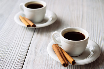 Two cups of coffee with cinnamon sticks on a white wooden table