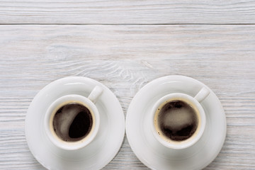 Two cups of coffee with foam on a white wooden table