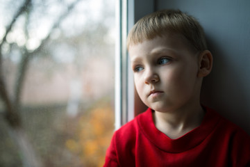 small boy sitting near window and thnking about something