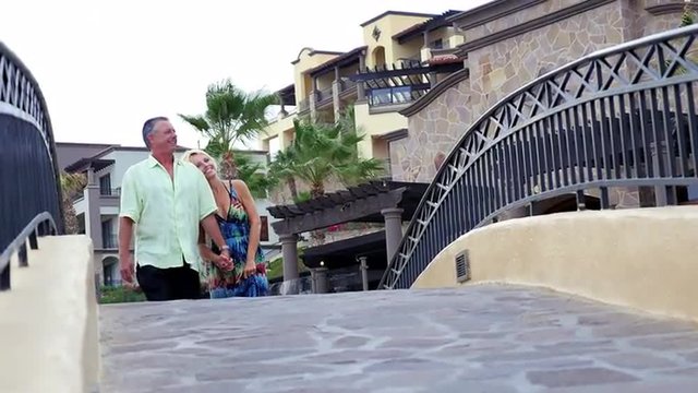 An older couple holding hands and walking over a small bridge at a resort