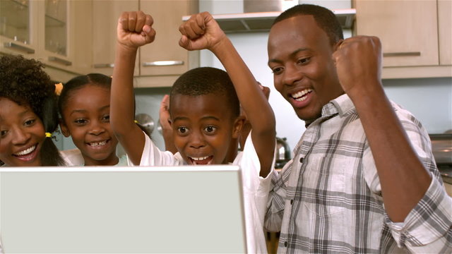 Happy black family rejoicing and using laptop