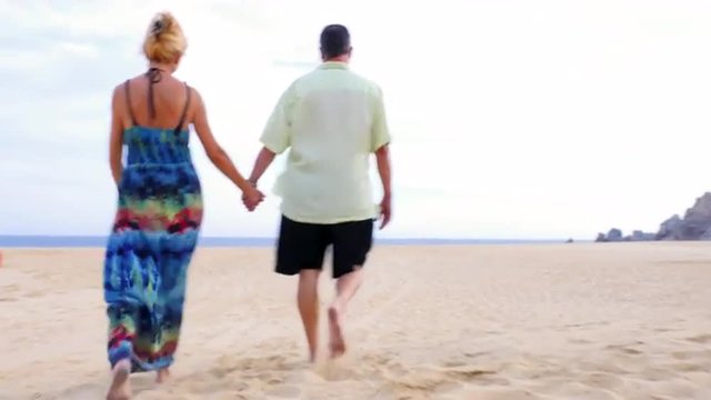 An older couple holding hands and walking on the beach 