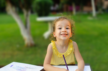 cute happy little girl drawing something in her notebook at the garden.